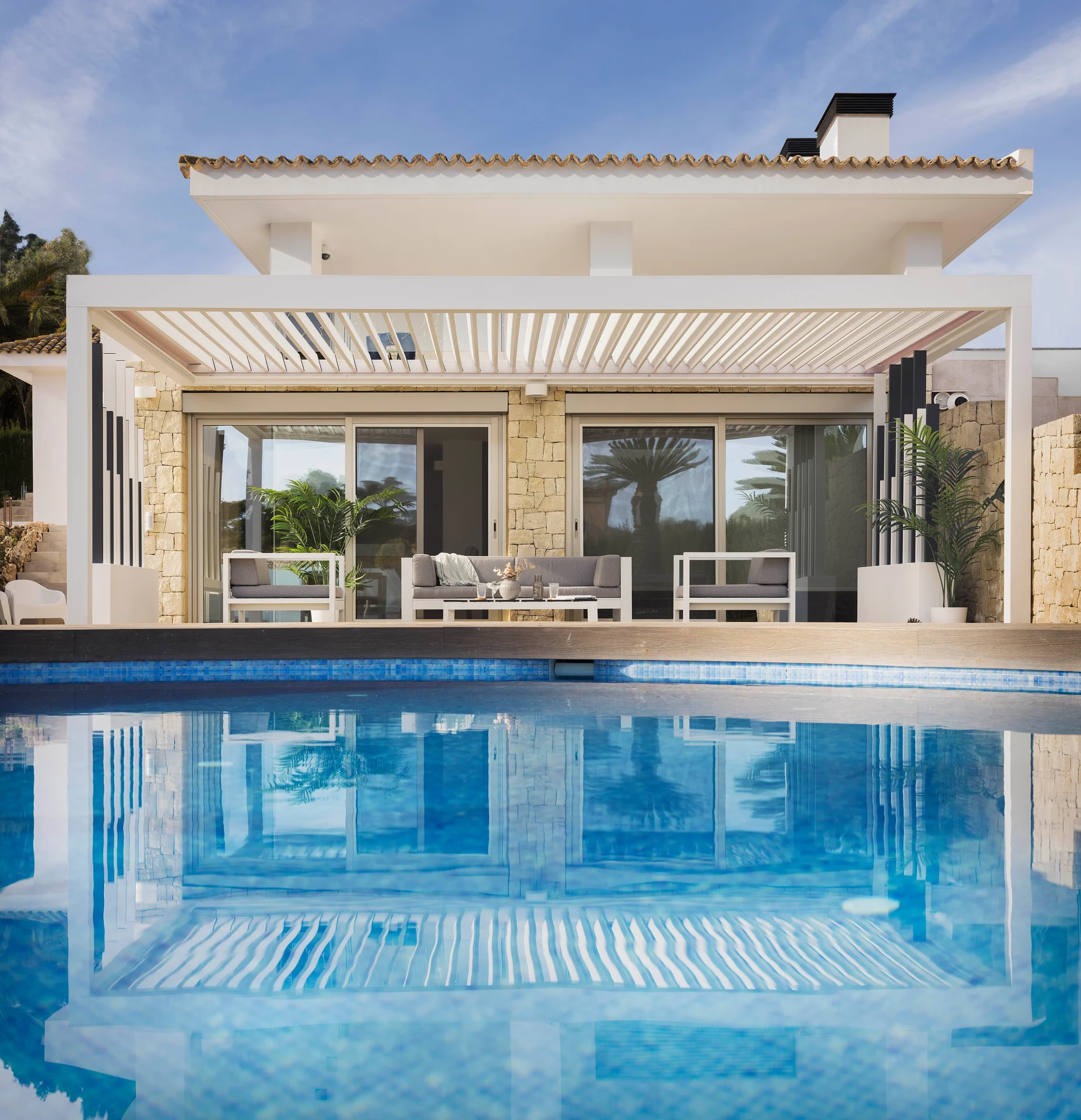 Pérgola branca com lâminas orientáveis sobre uma zona de estar junto à piscina